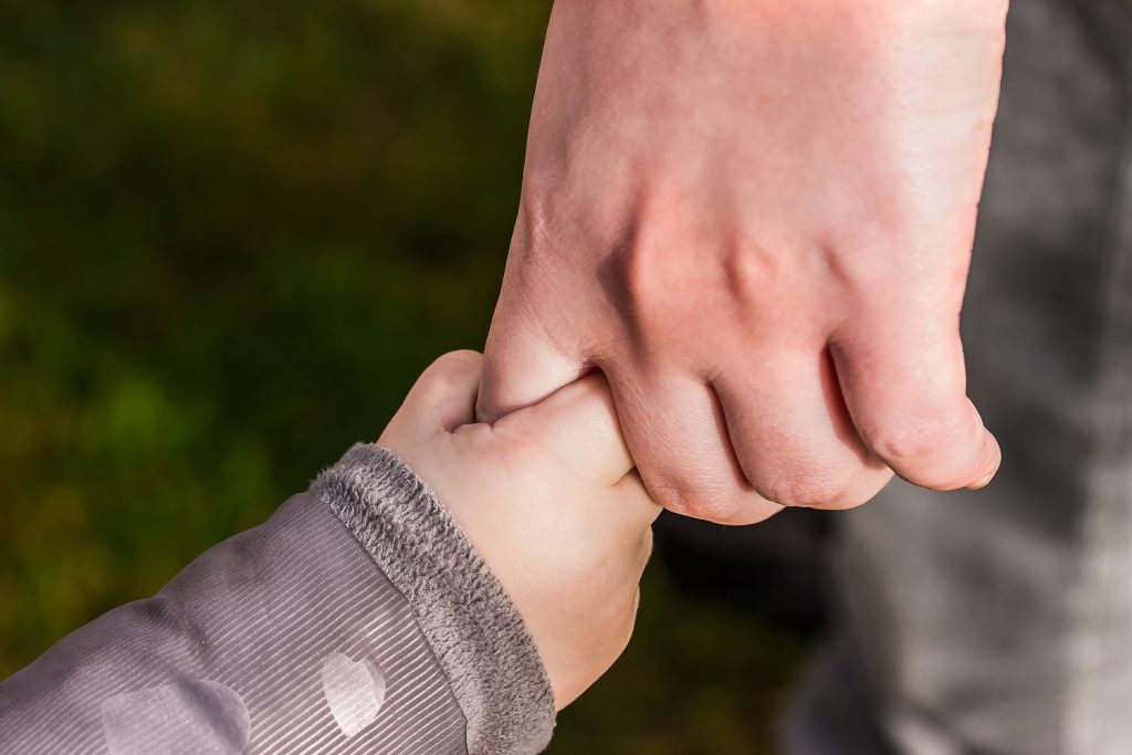 Kinderhand haelt die Hand eines Erwachsenen – Kontakt zum Kind nach der Inobhutnahme